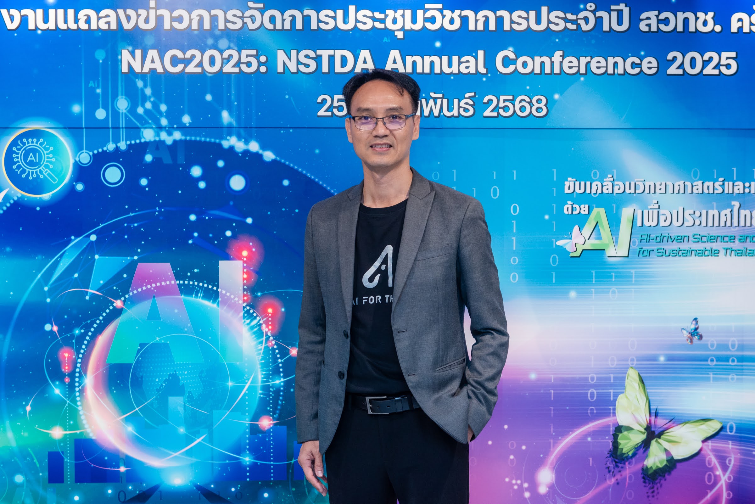 ภาพดร.ชัย วุฒิวิวัฒน์ชัย ผู้อำนวยการศูนย์เทคโนโลยีอิเล็กทรอนิกส์และคอมพิวเตอร์แห่งชาติ (เนคเทค) มีฉากหลังเป็นผีเสื้อและ ai ที่เป็นสัญลักษณ์หลักของงานในครั้งนี้
