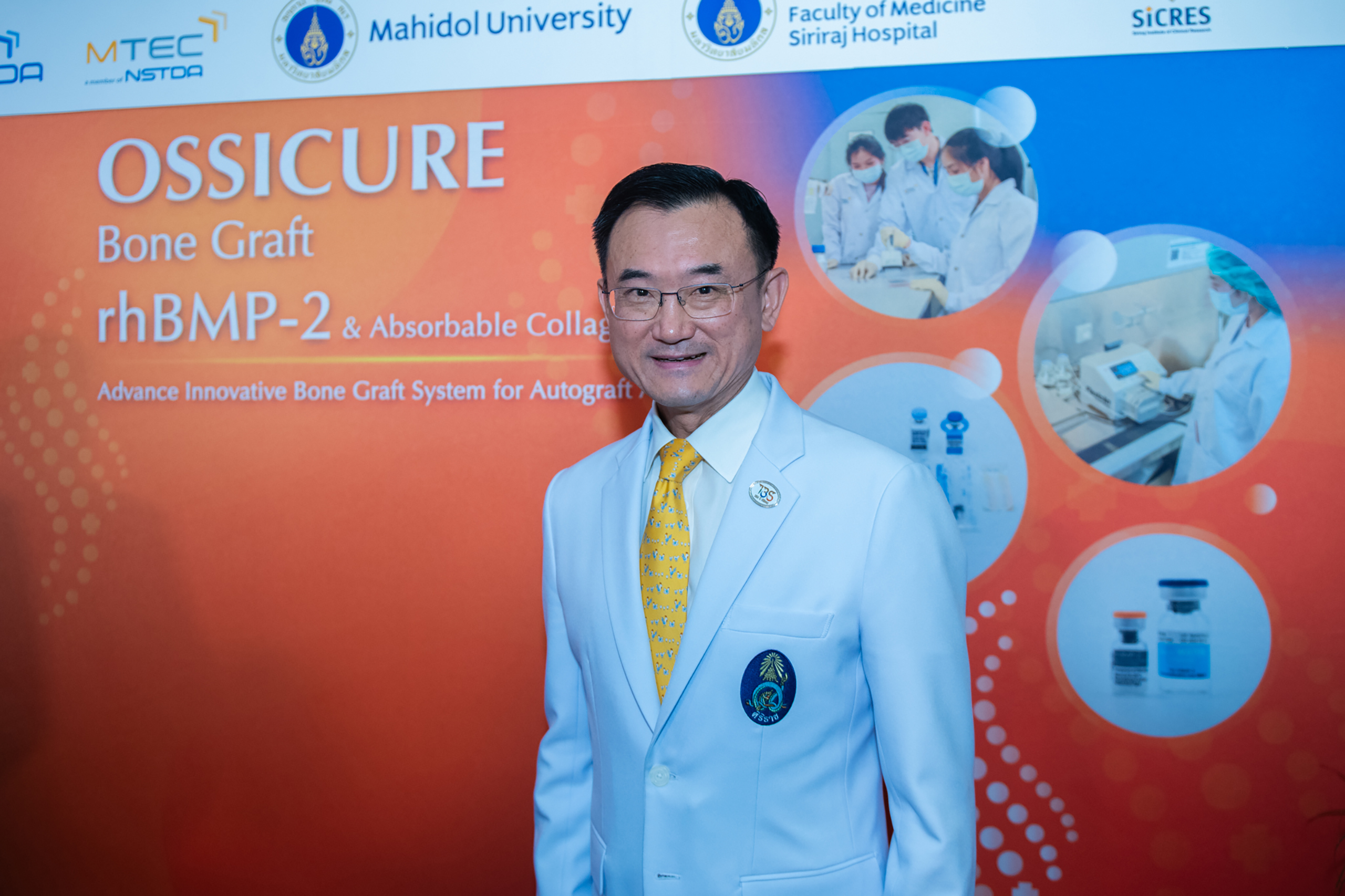 ภาพศาสตราจารย์ นายแพทย์อภิชาติ อัศวมงคลกุล คณบดีคณะแพทยศาสตร์ศิริราชพยาบาล มหาวิทยาลัยมหิดล ด้านหลังเป็น backdrop ผลงาน OSSICURE Bone Graft