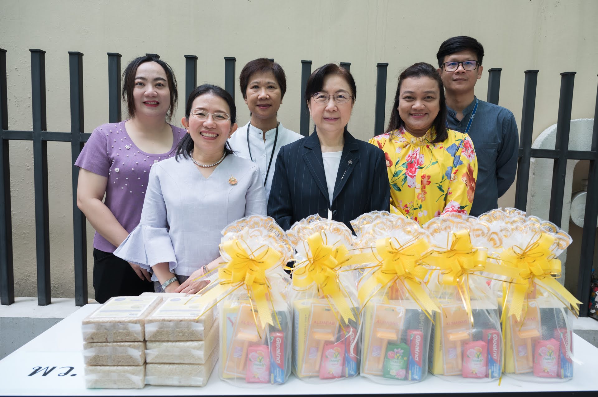 ภาพเจ้าหน้าที่จากหน่วยงานในสังกัดกระทรวง อว. ยืนถ่ายภาพร่วมกันหน้าโต๊ะที่จัดเตรียมชุดของถวายและของแห้ง สำหรับพิธีทำบุญตักบาตรเนื่องในวันสถาปนากระทรวง อว. ครบรอบ 6 ปี