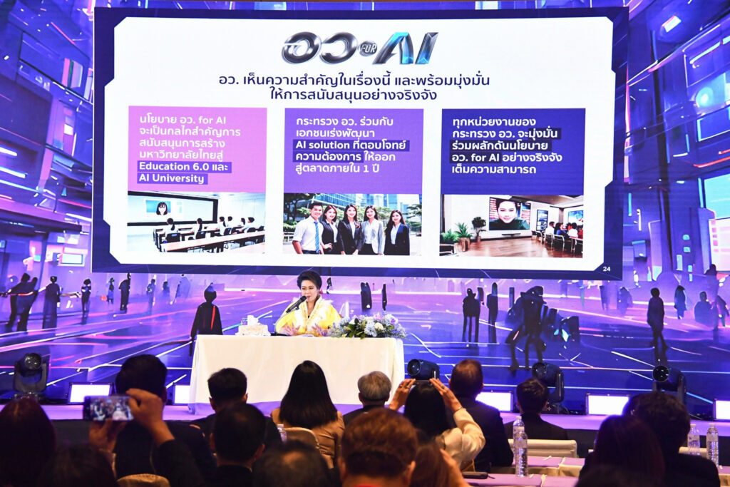 ภาพ น.ส.ศุภมาส อิศรภักดี รมต.อว. นั่งเก้าอี้ที่มีโต๊ะพร้อมพุ่มดอกไม้บนเวที กำลังพูดถึงเรื่อง อว. For AI ซึ่งโชว์บนจอ LED ด้านหลัง