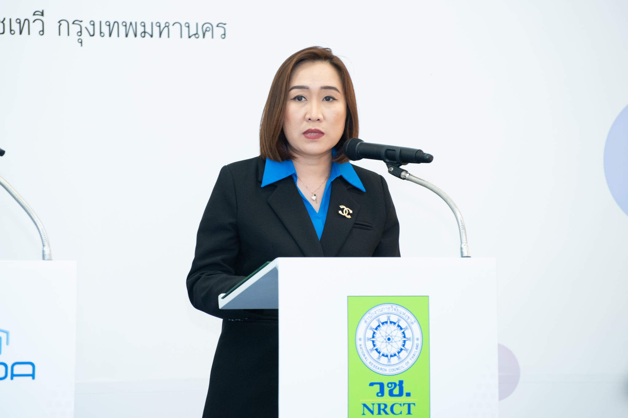 ภาพ คุณศิรินทร์พร เดียวตระกูล ผู้เชี่ยวชาญด้านระบบวิจัย วช. กล่าว ภารกิจหลักของ วช. ตรงโพเดียมสีขาว บนเวที
