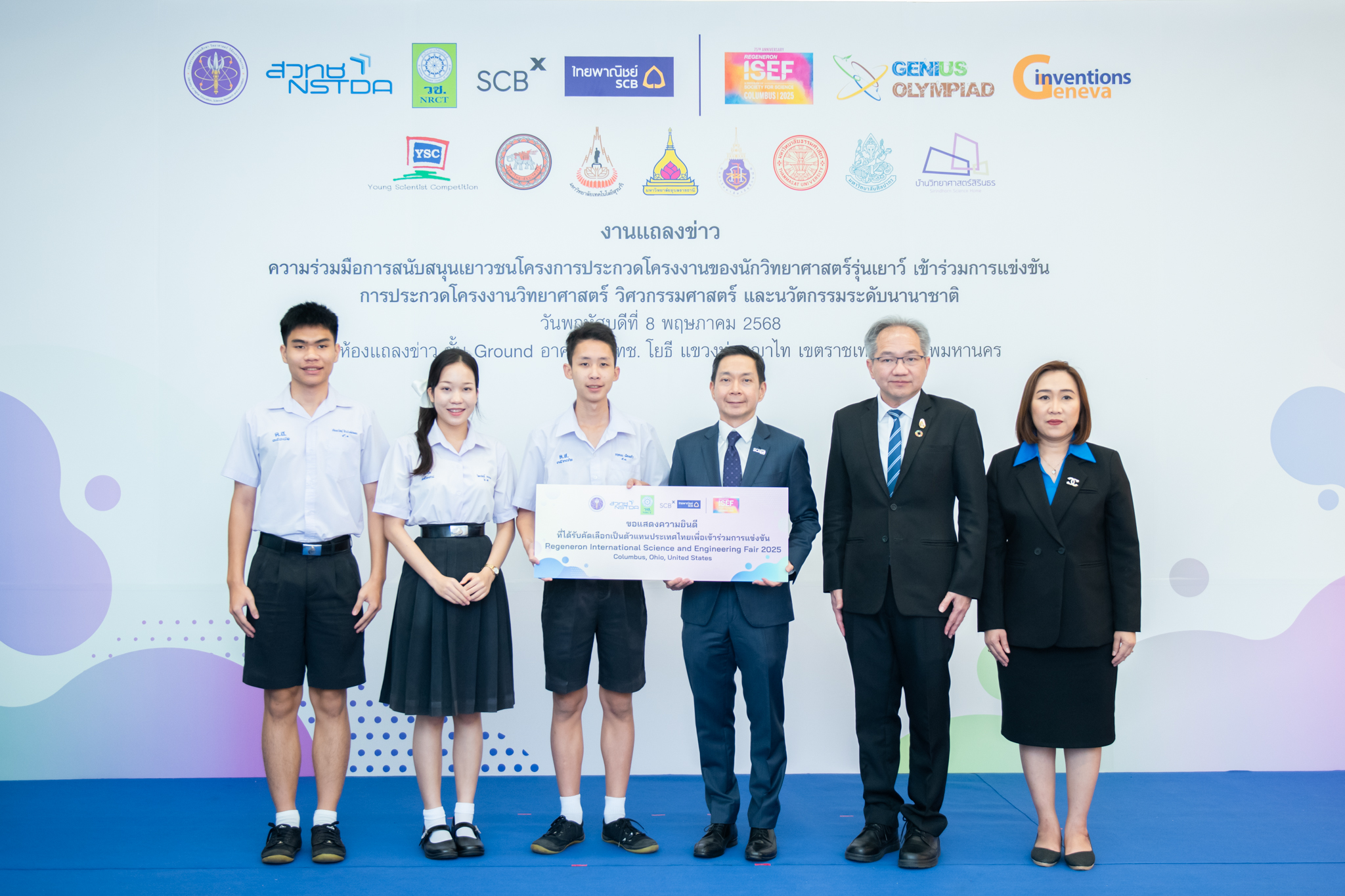 ภาพถ่ายนี้ มีบุคคลทั้งหมด 6 คน ยืนเรียงแถวหน้าฉากหลังที่เป็นแผ่นป้ายงานแถลงข่าว มีนักเรียน 3 คน ชาย 2 คน และหญิง 1 คน ในชุดนักเรียนมัธยมปลาย ถือแผ่นป้ายขนาดใหญ่สีขาวเขียนชื่อรางวัล กับผู้บริหาร วช. สวทช SCB ใส่สูทแบบอย่างการ ทุกคนในภาพยิ้มแย้ม ยืนใกล้กันอย่างเป็นทางการ