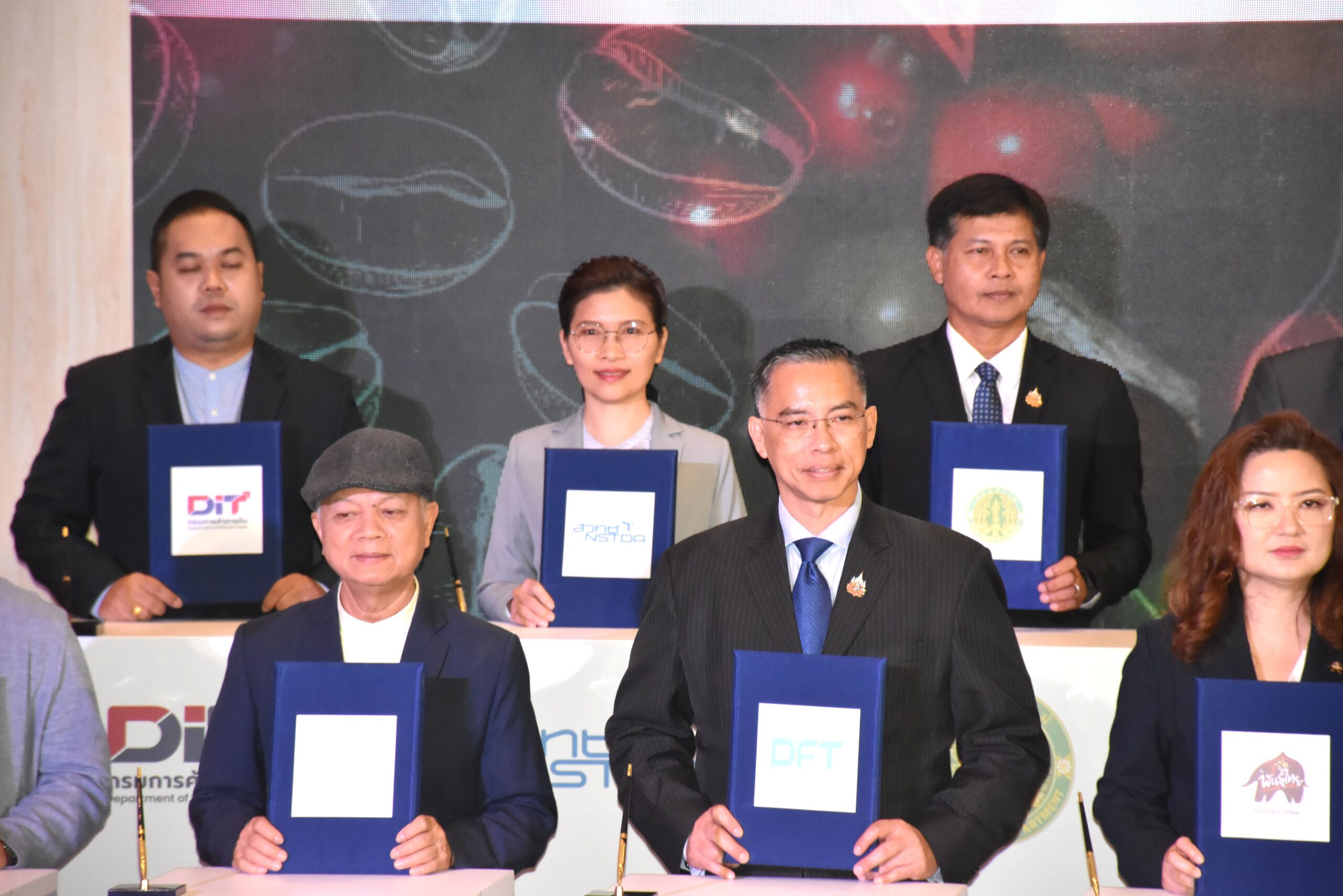 ภาพครึ่ง ผู้ช่วยศาสตราจารย์ ดร.เชาวรีย์ อรรถลังรอง ผู้อำนวยการ ไบโอเทค สวทช. ยืนตรงกลางตรงโพเดียม ถือป้ายชื่อ สวทช. และมีผู้บริหารท่านอื่นยืนข้างๆ