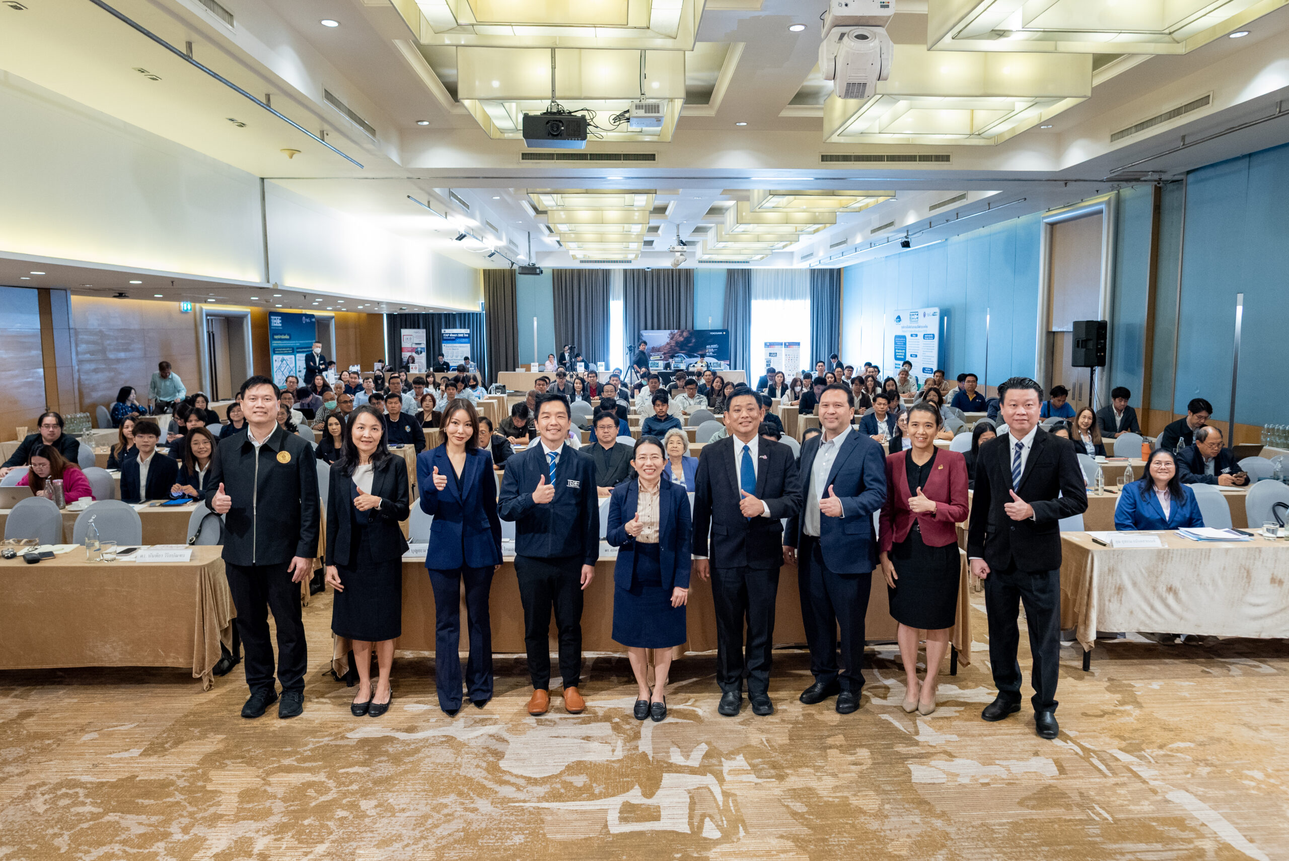 ภาพหมู่ ผู้บริหาร สวทช. TECE สภาอุตสาหกรรมแห่งประเทศไทย สถาบันยานยนต์ ยืนอยู่ด้านหน้าของผู้เข้าร่วมสัมนนาที่นั่งโต๊ะ สวมชุดสูท พร้อมด้วยท่ากดไลท์