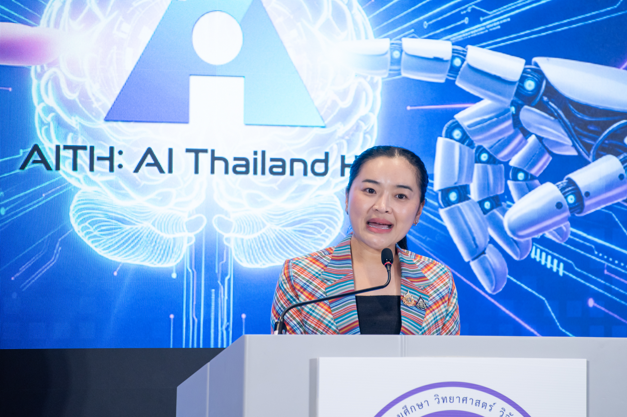 นางสาวสุดาวรรณ หวังศุภกิจโกศล รัฐมนตรีว่าการกระทรวง อว. กล่าวแสดงความยินดีในพิธีลงนามความร่วมมือเตรียมการจัดตั้ง AI Thailand Hub ชุดเสื้อสูทลายผ้าขาวม้า 