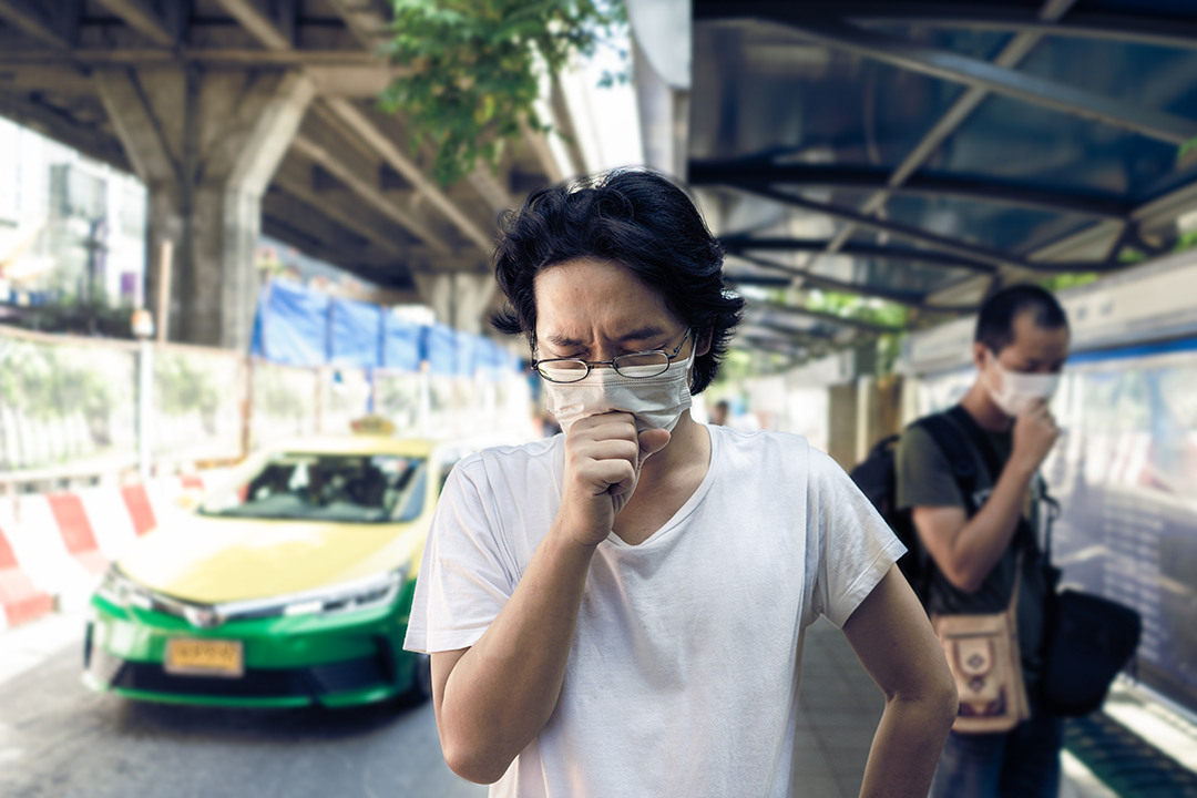 ภาพผู้ชายสวมมาสก์กำลังไอขณะเดินบนท้องถนน เนื่องจากมลพิษฝุ่น PM2.5
