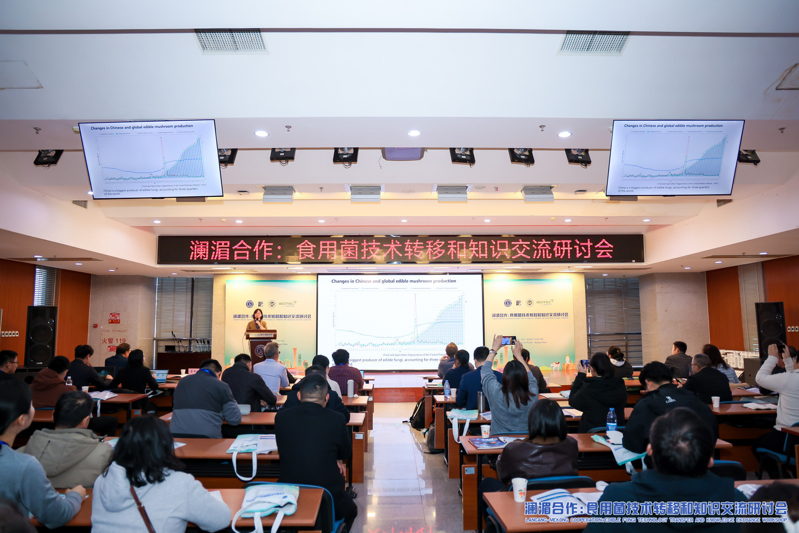 ภาพบรรยากาศการบรรยายในงาน Workshop ด้านเทคโนโลยีเห็ดกินได้ ผู้เข้าร่วมกำลังนั่งฟังการนำเสนอที่มีกราฟการผลิตเห็ดของจีนและโลกแสดงบนหน้าจอ