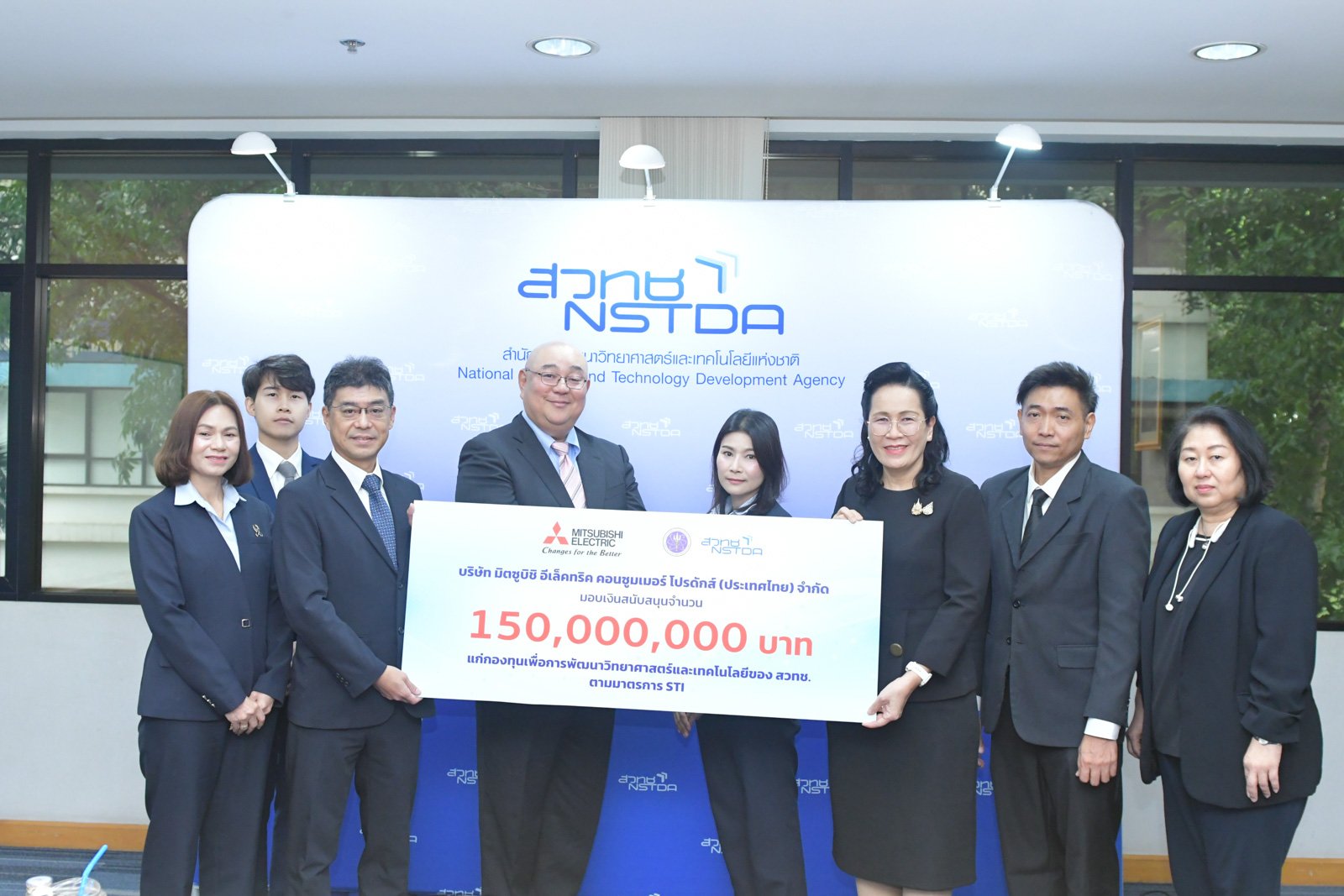 ภาพผู้แทนจากบริษัทเอกชนส่งมอบป้ายเงินสนับสนุนมูลค่า 150 ล้านบาท ให้กับผู้แทน สวทช. ณ ฉากหลังโลโก้ NSTDA