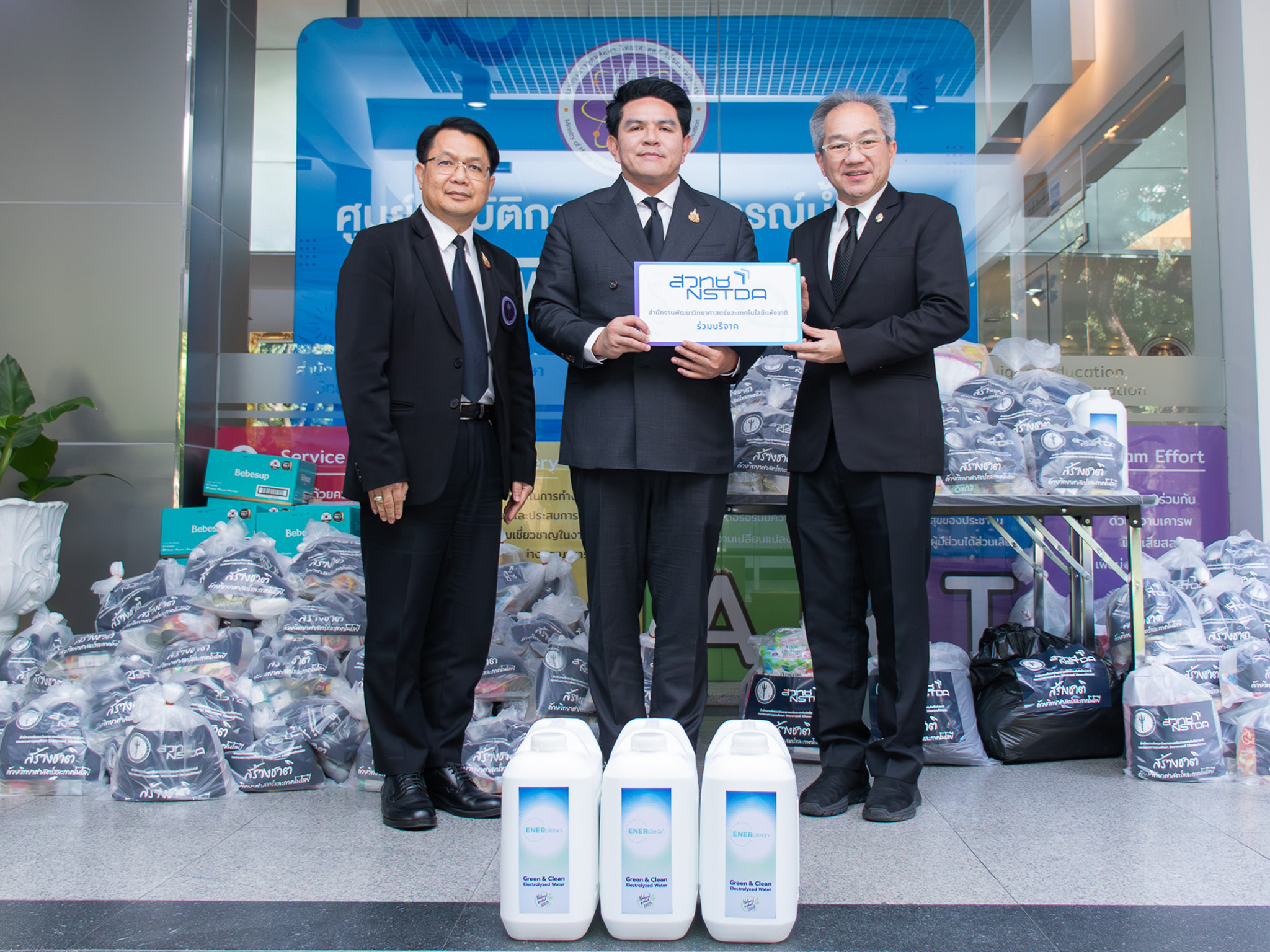 ภาพตัวแทน สวทช. ส่งมอบถุงยังชีพและน้ำยาฆ่าเชื้อ ENERclean ให้ศูนย์ปฏิบัติการสถานการณ์น้ำท่วม อว. โดยมีถุงยังชีพและน้ำยาฆ่าเชื้อจัดวางอยู่ด้านหลัง