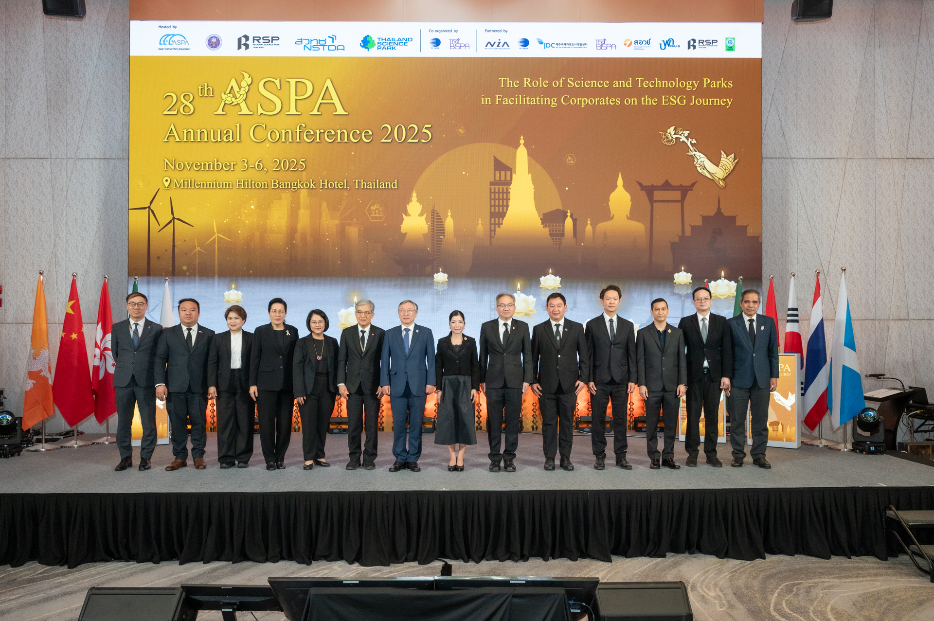 ภาพหมู่ ผู้บริหาร ถ่ายภาพบนเวที สวมใส่สูทสีดำ ด้านหลังเป็น Backdrop งาน ASPA 2025 ธีมสีทอง ส้มเป็นภาพวัดของกรุงเทพ เสาชิงช้า แล้วมีการลอยกระทง