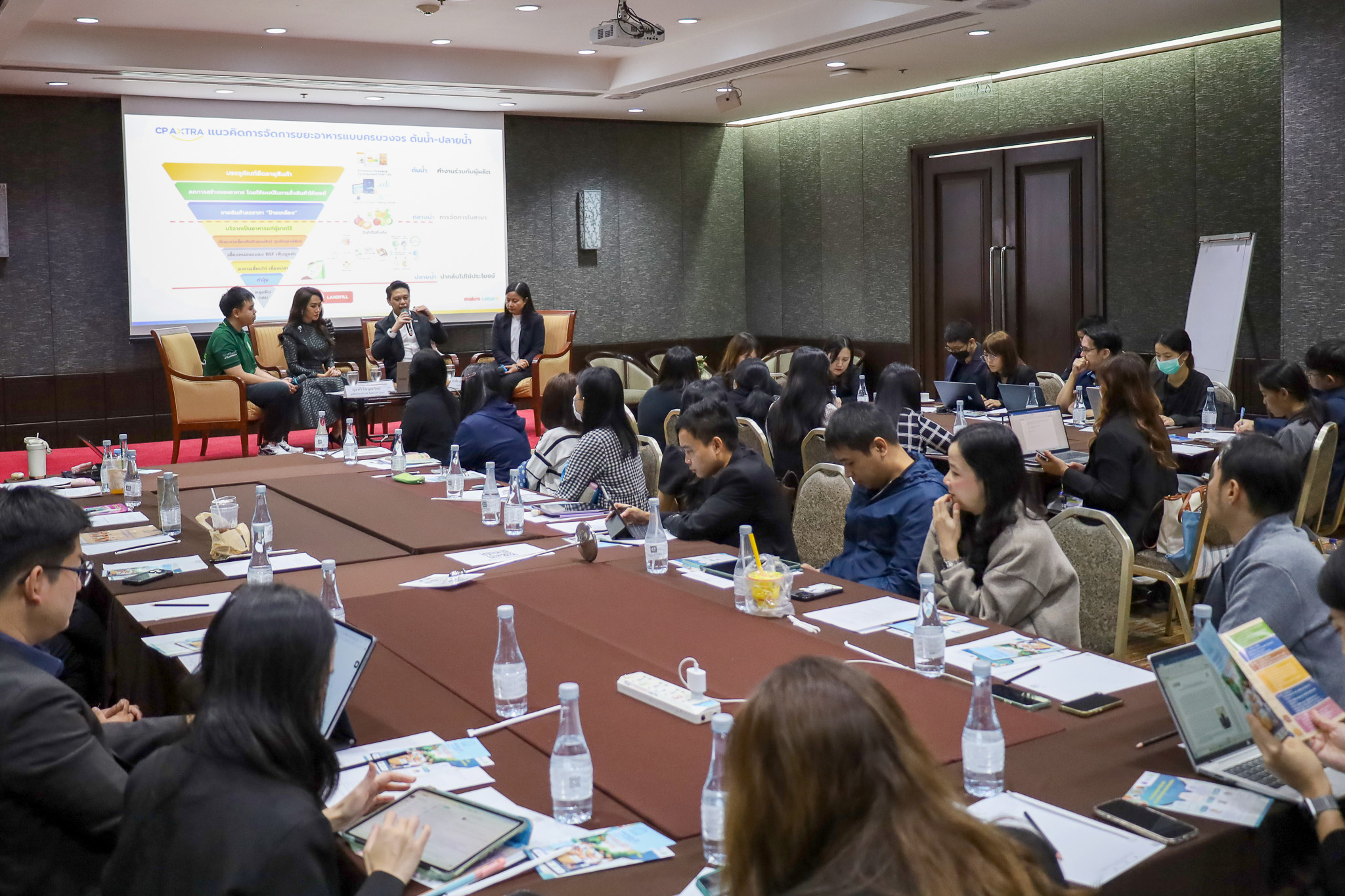 ภาพการเสวนาบนเวที ขณะผู้เข้าร่วมประชุมจำนวนมากกำลังรับฟังและบันทึกข้อมูล