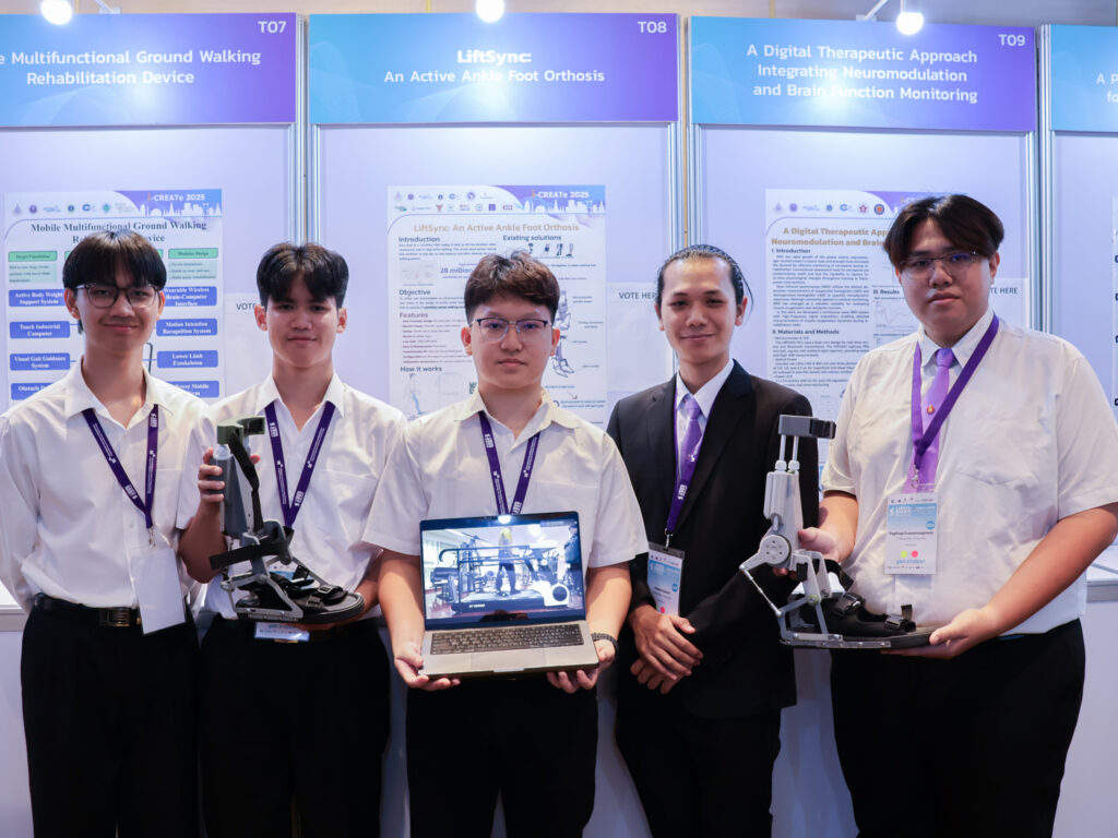 ภาพ นักศึกษายืนถือผลงานจากการประกวดสิ่งประดิษฐ์สำหรับคนพิการและผู้สูงอายุ ของบูธนิทรรศการ ในงาน