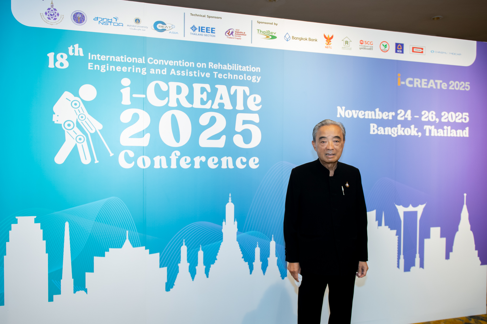 ภาพ ศาสตราจารย์ ดร.ไพรัช ยืนหน้า Backdrop งาน ธีมฟ้าม่วง