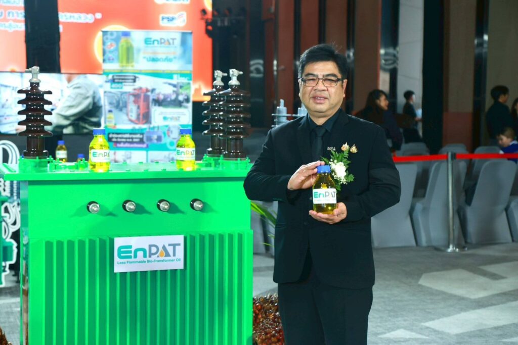 ภาพ: นายดิเรก บุญปิยทัศน์ รองผู้ว่าการ กฟน. ถือขวดน้ำมัน EnPAT ยืนถ่ายภาพคู่กับโมเดลหม้อแปลงไฟฟ้าสีเขียวภายในงานแถลงข่าว