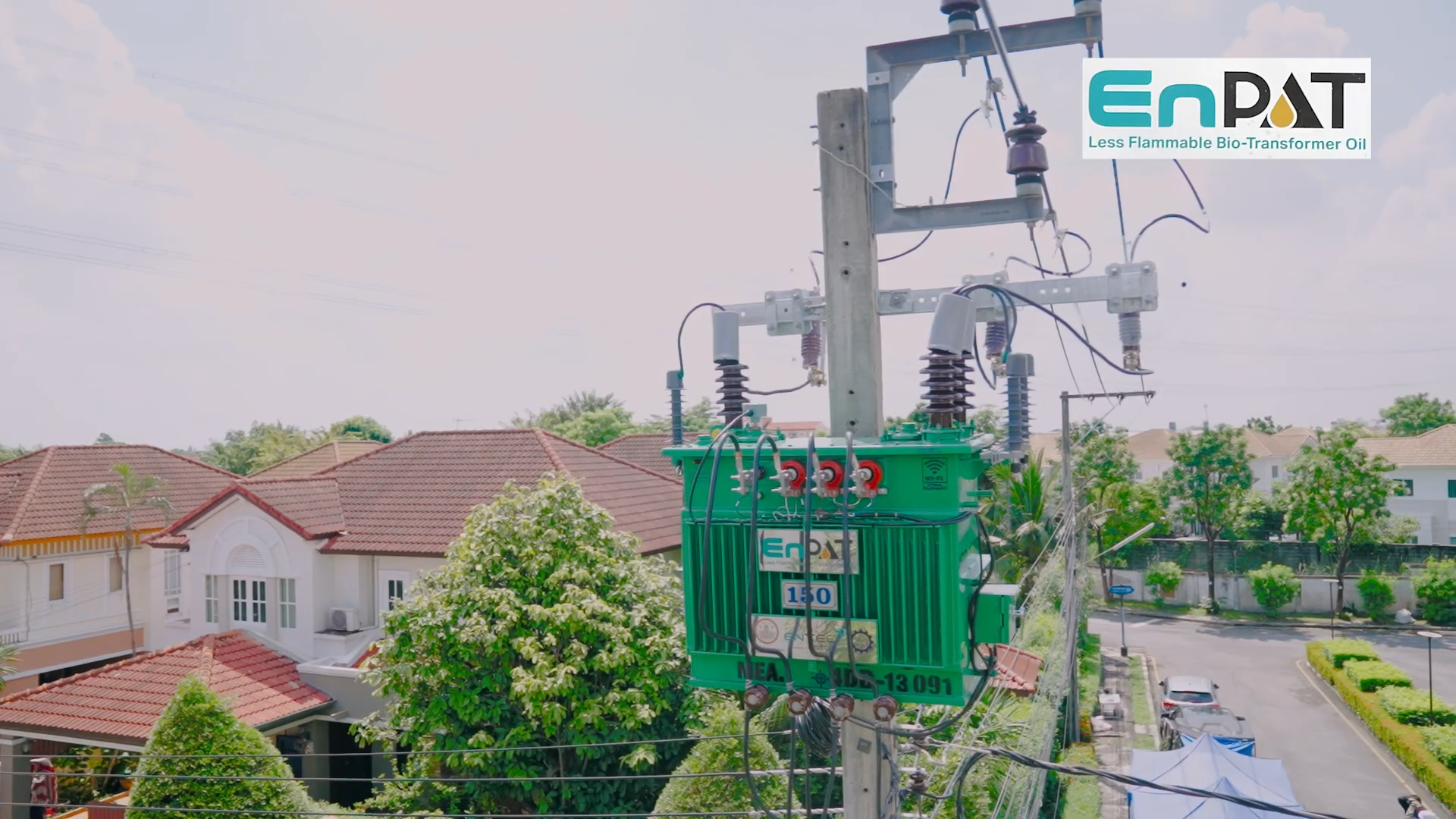 ภาพ: หม้อแปลงไฟฟ้าสีเขียวระบุสัญลักษณ์ EnPAT ติดตั้งอยู่บนเสาไฟฟ้าท่ามกลางสภาพแวดล้อมที่เป็นย่านที่อยู่อาศัยที่มีต้นไม้ปกคลุม