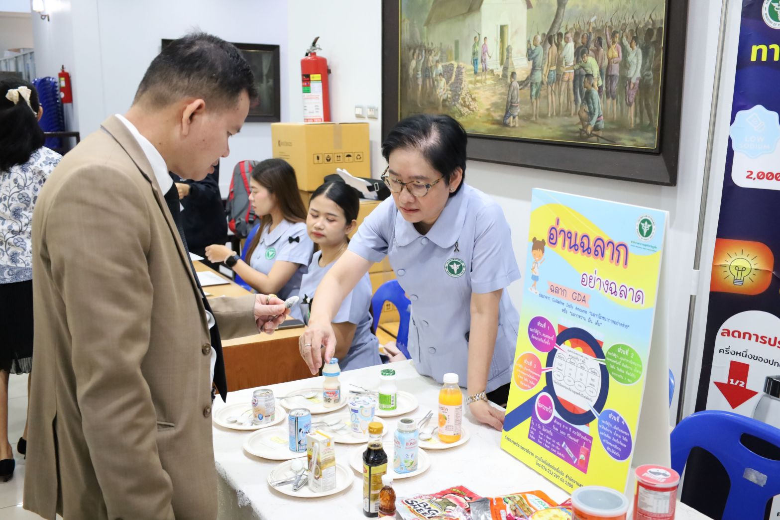 ภาพ: เจ้าหน้าที่สาธารณสุขกำลังให้ความรู้เรื่องโภชนาการและการอ่านฉลากอาหาร (ฉลาก GDA) แก่ผู้เข้าร่วมงาน โดยมีตัวอย่างผลิตภัณฑ์อาหารและเครื่องดื่มจัดแสดงเพื่อเปรียบเทียบปริมาณน้ำตาลและโซเดียม
