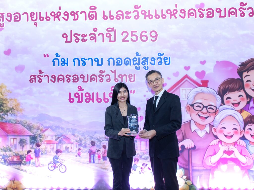 ภาพ นักวิจัย ถ่ายภาพกับ ดร.สมบุญ สหสิทธิวัฒน์ หน้าป้ายงานวันผู้สูงอายุแห่งชาติและวันครอบครัว ประจำปี 2569